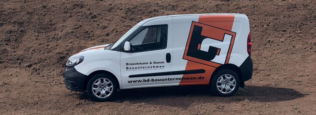 Kompakter weißer Firmenwagen mit auffälliger Fahrzeugbeschriftung von „Brauckmann & Damm Bauunternehmen“. Das Design zeigt ein großes stilisiertes „B+D“-Logo in Schwarz und Orange sowie die Website „www.bd-bauunternehmen.de“. Der Wagen steht auf braunem Erdboden.