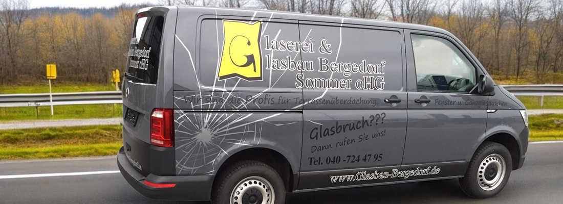Ein grauer Lieferwagen mit dem Firmennamen „Glaserei & Glasbau Bergedorf Sommer oHG“ an der Seite. Das Design zeigt eine Grafik mit einem Glasbrucheffekt und unterstreicht die Leistungen der Firma im Bereich Glasreparatur. Der Lieferwagen parkt am Straßenrand. Im Hintergrund sind Grünflächen und Bäume zu sehen, die eine typische Stadtlandschaft abbilden. Kontaktinformationen und eine Website-URL sind ebenfalls am Fahrzeug sichtbar.